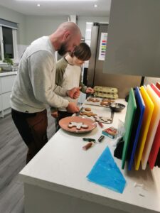 Sam, a man with autism and Down syndrome, smiling while decorating gingerbread men in the warm, modern kitchen of his new independent home